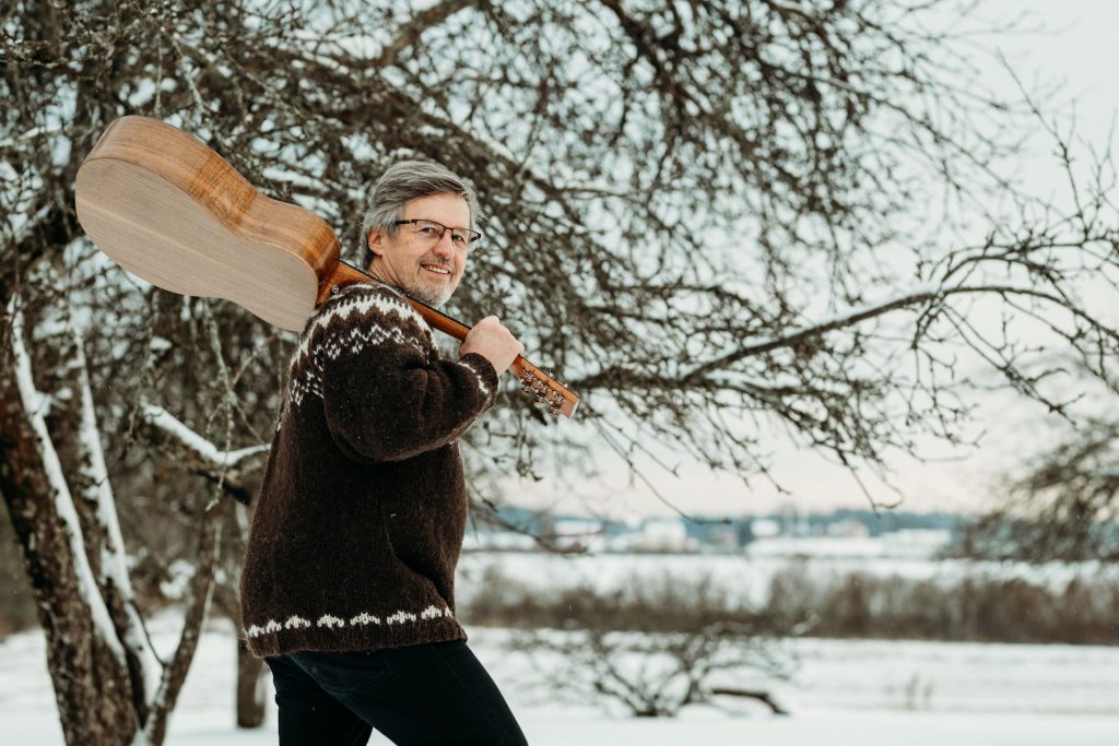 Kuvassa Pekka Simojoki puun edessä kitara olalla.